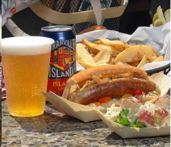 A beer beside a hotdog.